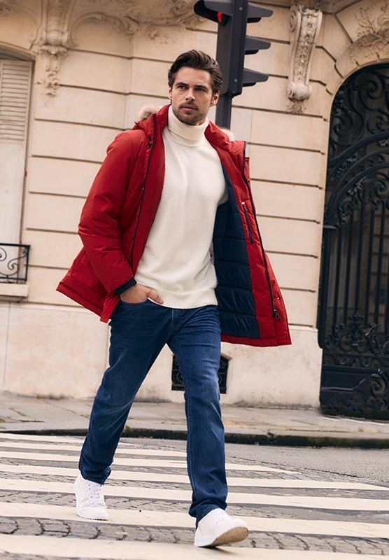 Mann mit weißem Rollkragenpullover, Jeans und rotem Winterparka